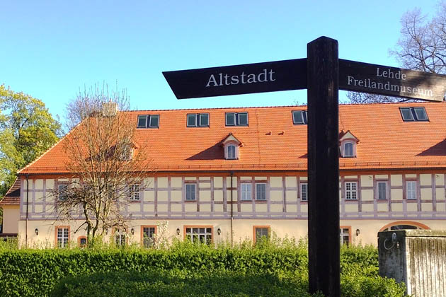 Der Marstall des Schloss Lübbenau, der heute Platz für Urlaubsgäste bietet, mit einem Wegweiser Richtung Altstadt und Spreewalddorf Lehde im Vordergrund. 